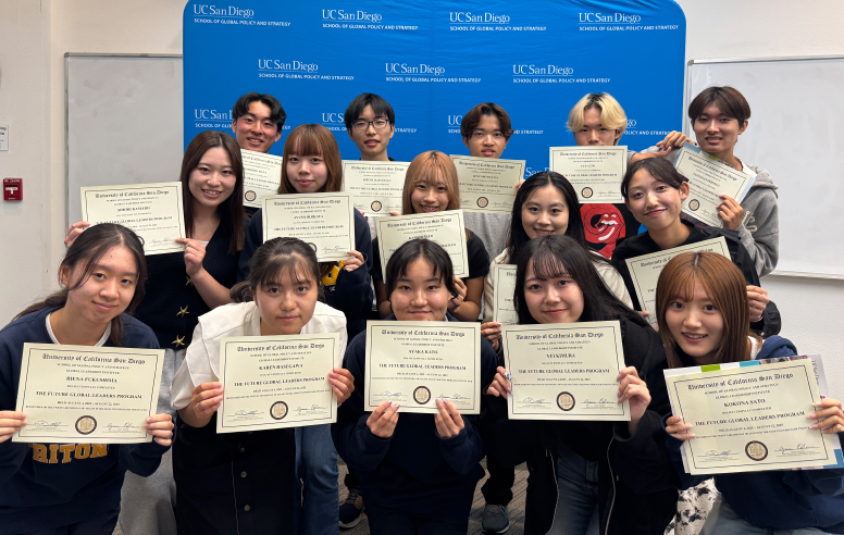 A group of diverse students smiling and holding up their certificates in front of a blue backdrop.