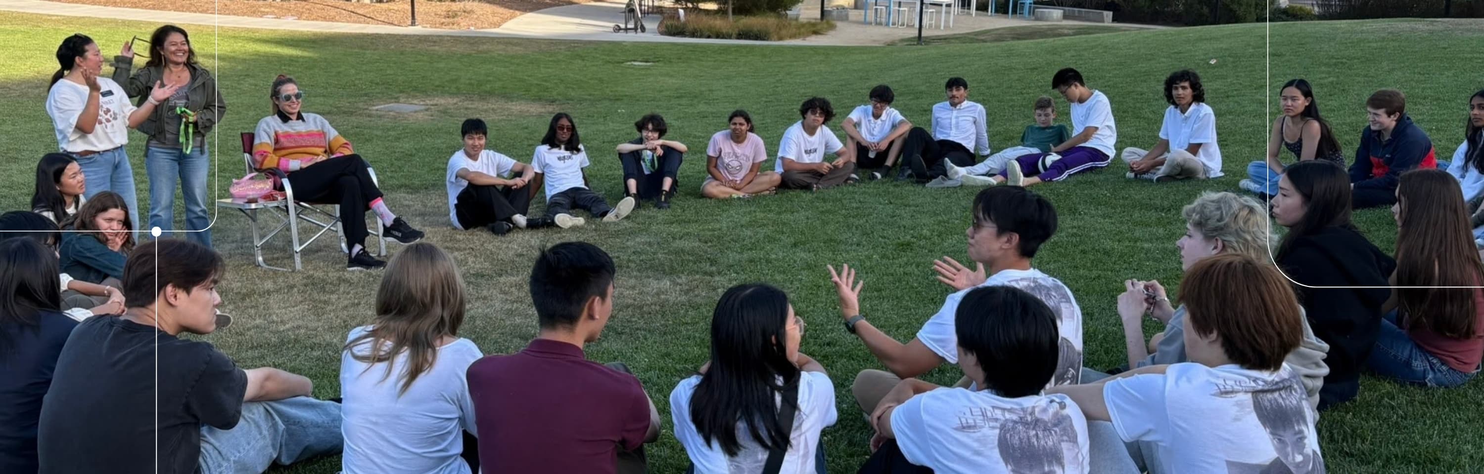 A large group of diverse students sitting in a circle on a grassy lawn during an outdoor discussion.