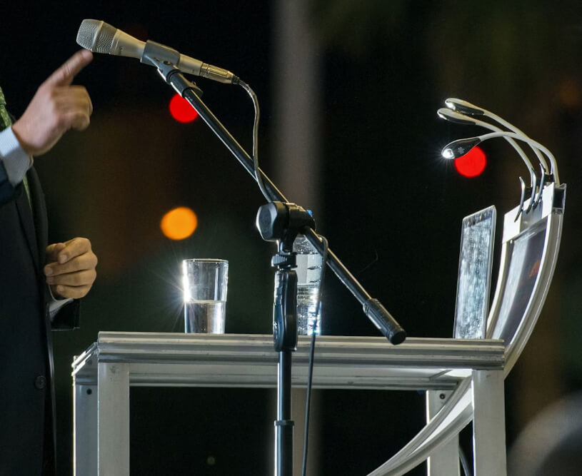 View of a podium and microphone setup with a person just off screen speaking